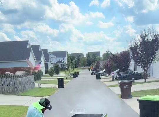 Pressure washing a neighborhood driveway with trash bins at the curb